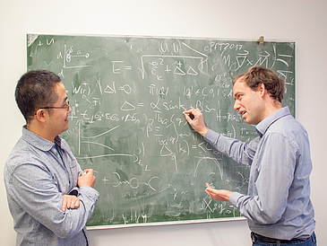 Zwei Männer stehen vor einer Tafel und diskutieren.