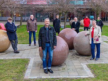 Men and women stand in front of large granite stone balls on a green area in front of a building