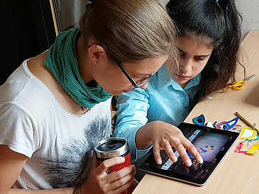 Zwei Mädchen sitzen am Tisch und schauen auf ein Tablet