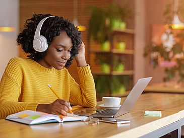 Junge Frau sitzt mit Kopfhörern vor dem Laptop